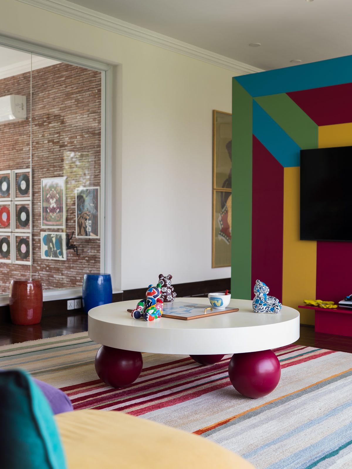 Round white table on red sphere legs before a colour-blocked wall in teal, magenta and yellow