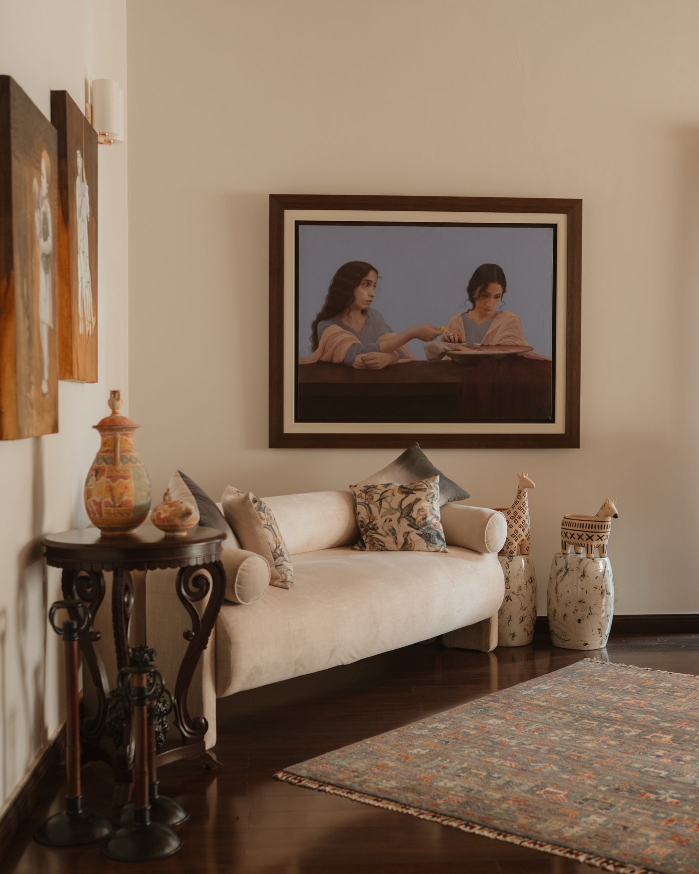 Ivory sofa beneath a painting of two figures, with a carved side table