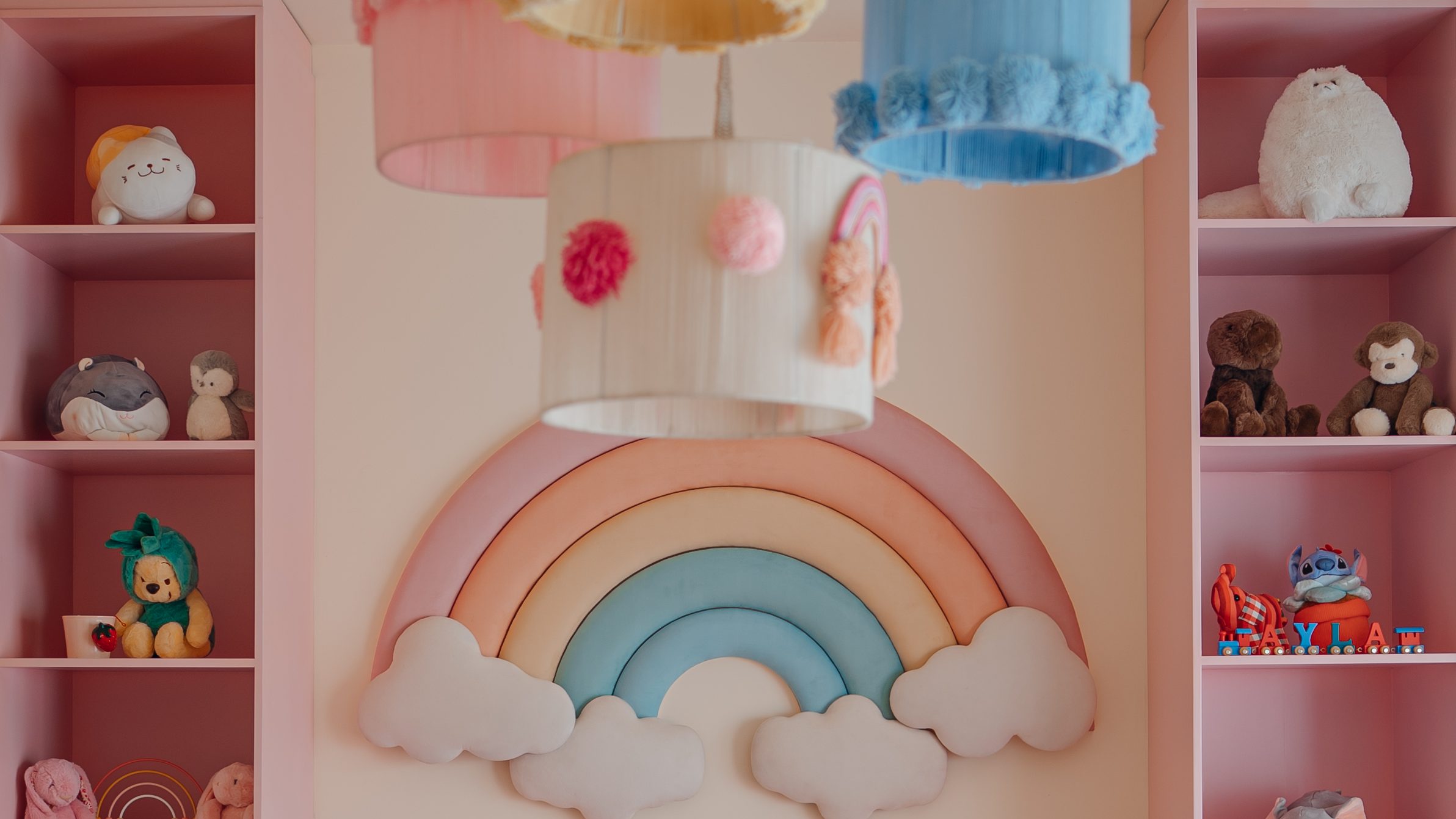 Pastel nursery with a padded rainbow, colour-blocked drawers and pompom pendant shades