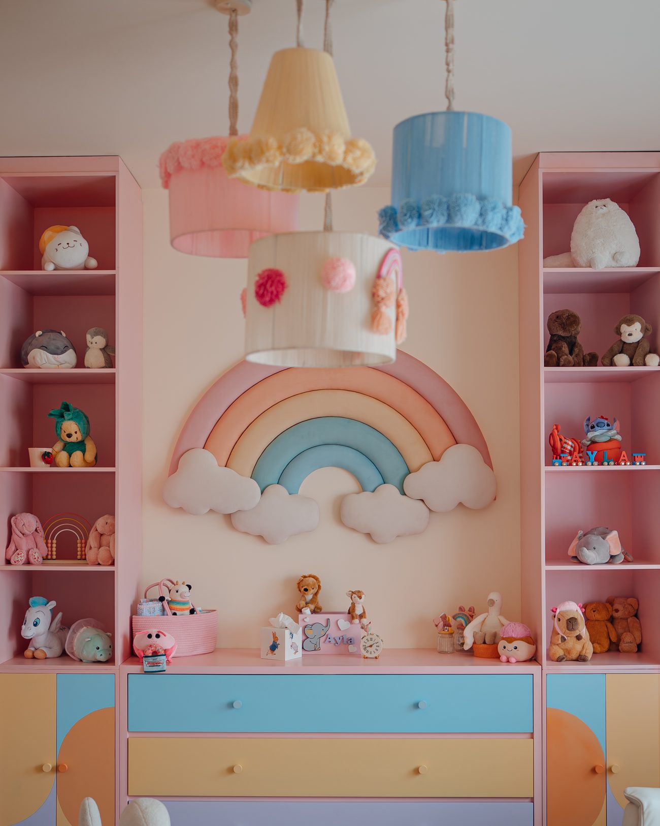 Pastel nursery with a padded rainbow, colour-blocked drawers and pompom pendant shades
