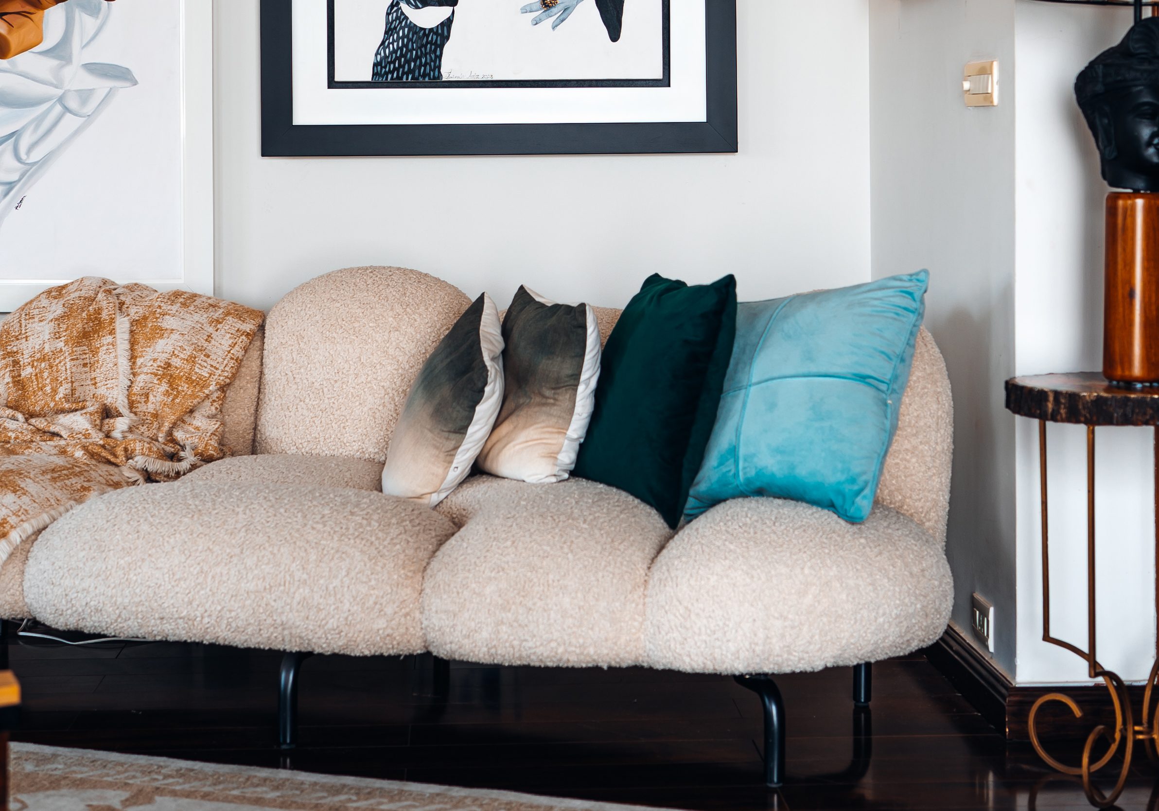 Bouclé sofa with velvet cushions beneath framed artwork