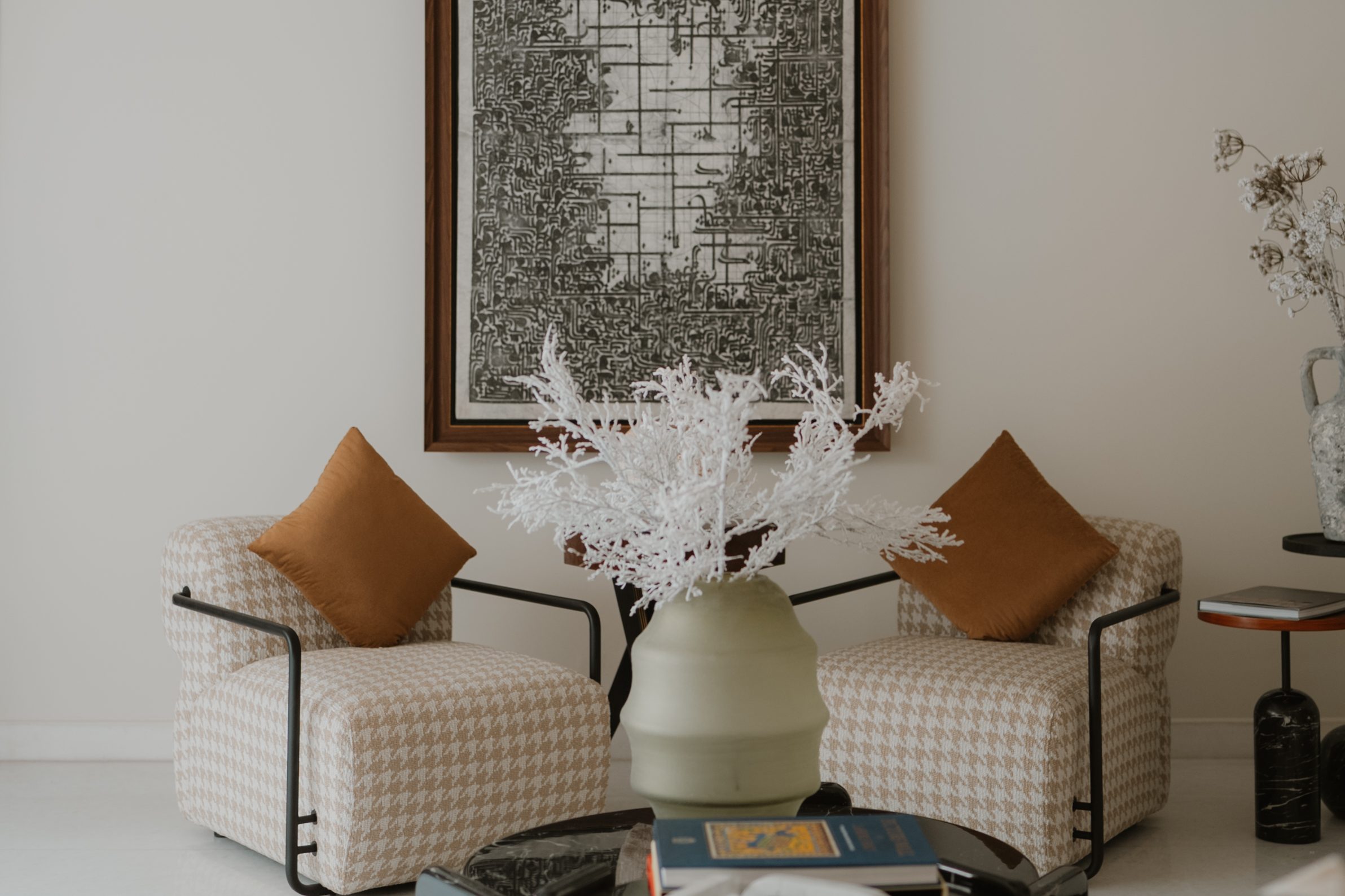 Houndstooth armchairs and white coral beneath the textured monochrome artwork