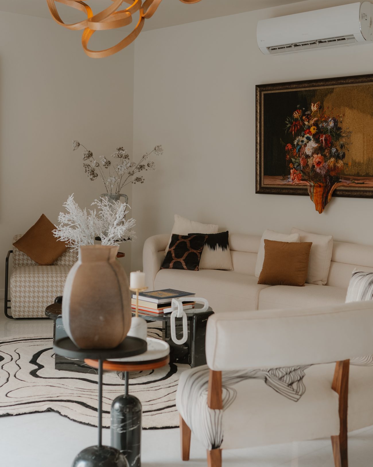 Pale lounge beneath the carved Raka light, with a stone vase on black marble tables and a contour rug