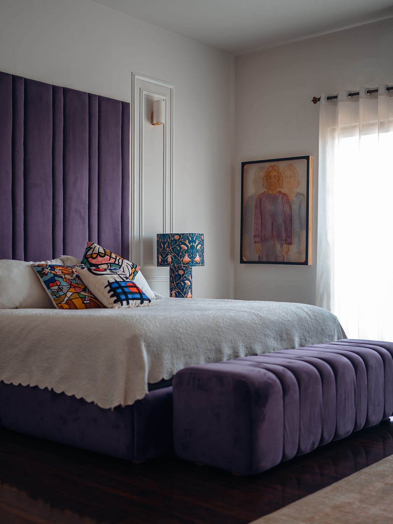 Bed with a purple channel-tufted headboard and matching bench, white bedding and patterned cushions