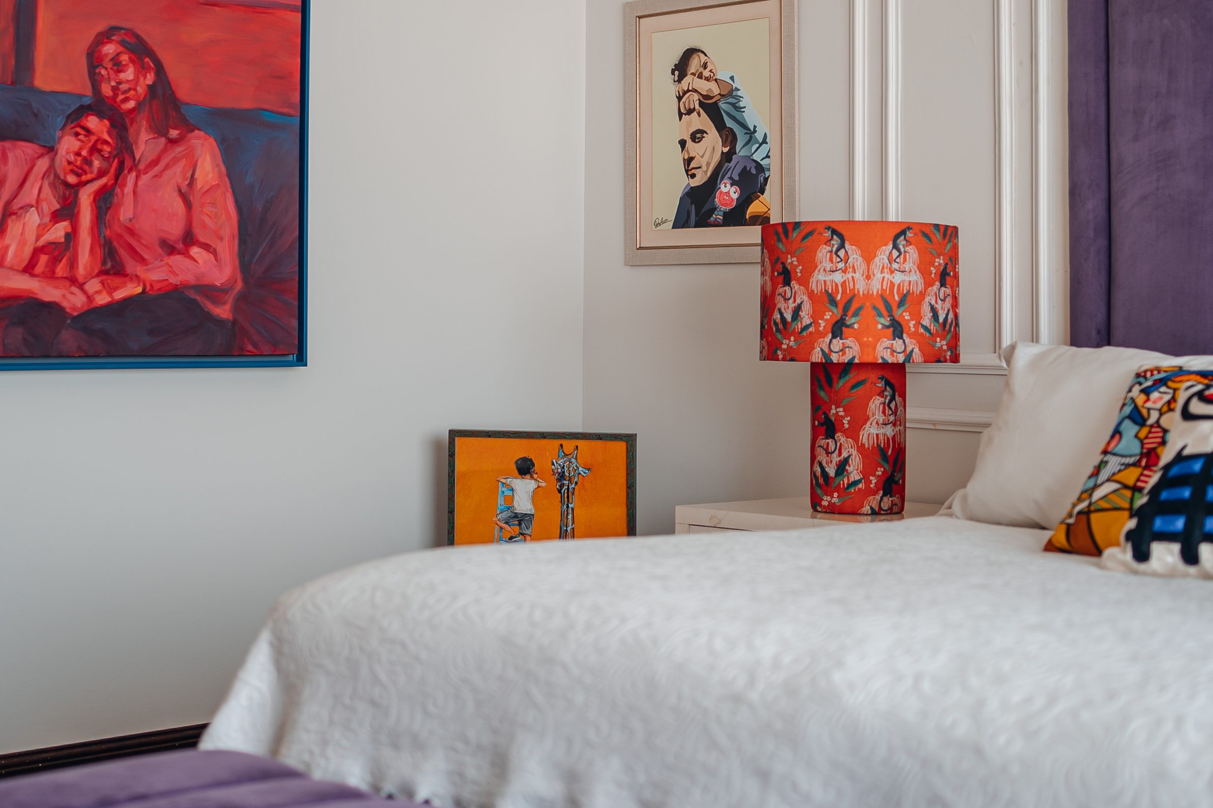 Bold paintings and a red lamp beside the bed