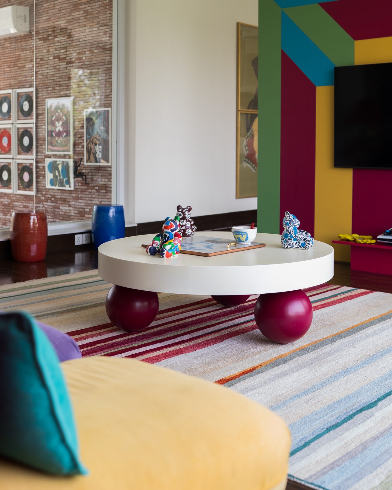 Colour-blocked wall in teal, magenta and yellow beside a round white table on red sphere legs