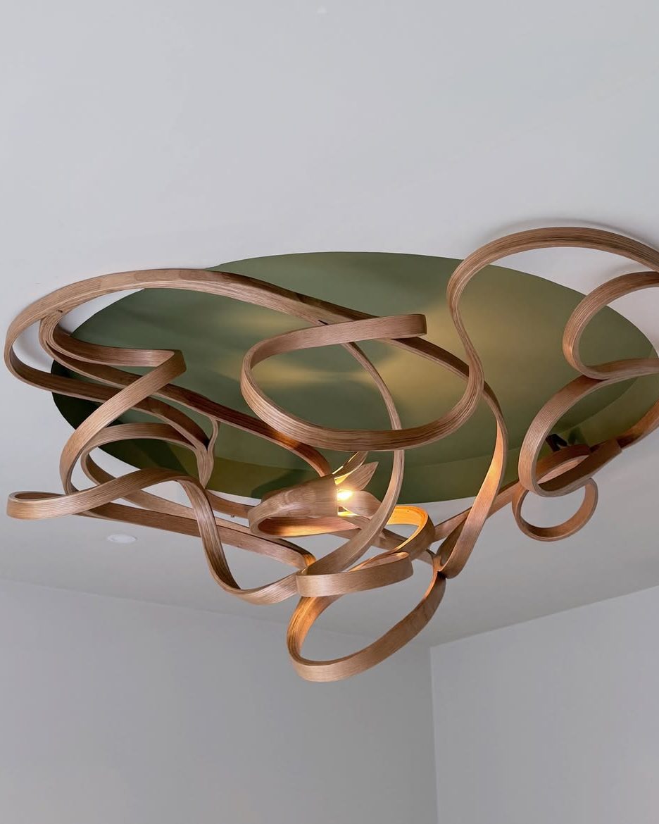 Carved timber ribbon light with a glowing centre, seen from below